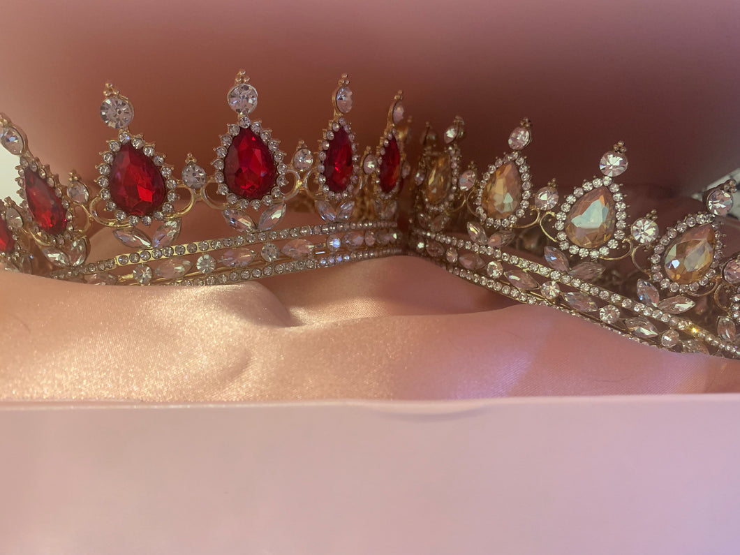 Two diamanté sparkling crowns, one set with oval champagne coloured stones and the other with faux rubies in a pink box with a silky pink lining inside the box and a pink bow to tie and secure the box closed.